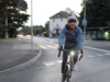 [Translate to Français:] Junge Frau auf der Strasse mit Velo unterwegs. Sie trägt einen Helm und das Velolicht scheint hell.